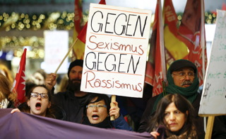 Women shout slogans and hold up a placard that reads "Against Sexism - Against Racism" as they march through the main railway station of Cologne