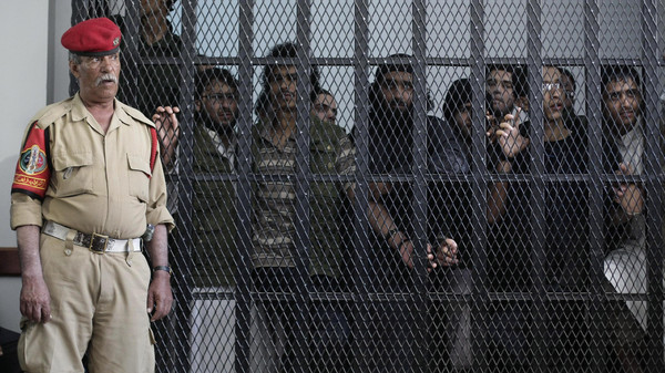 A Yemeni military policeman stands guard as suspected Yemeni militants stand behind bars during a court session at a state security court in Sanaa, Yemen, Wednesday, Oct. 2, 2013. Officials say the court Wednesday sentenced five militants to up to ten years in prison for their role in the May 2012 suicide attack that struck a military parade and killed more than 90 conscripts in the capital Sanaa. Three former top military officials, including a nephew of the former president, were accused of negligence in the suicide attack. (AP Photo/Hani Mohammed)