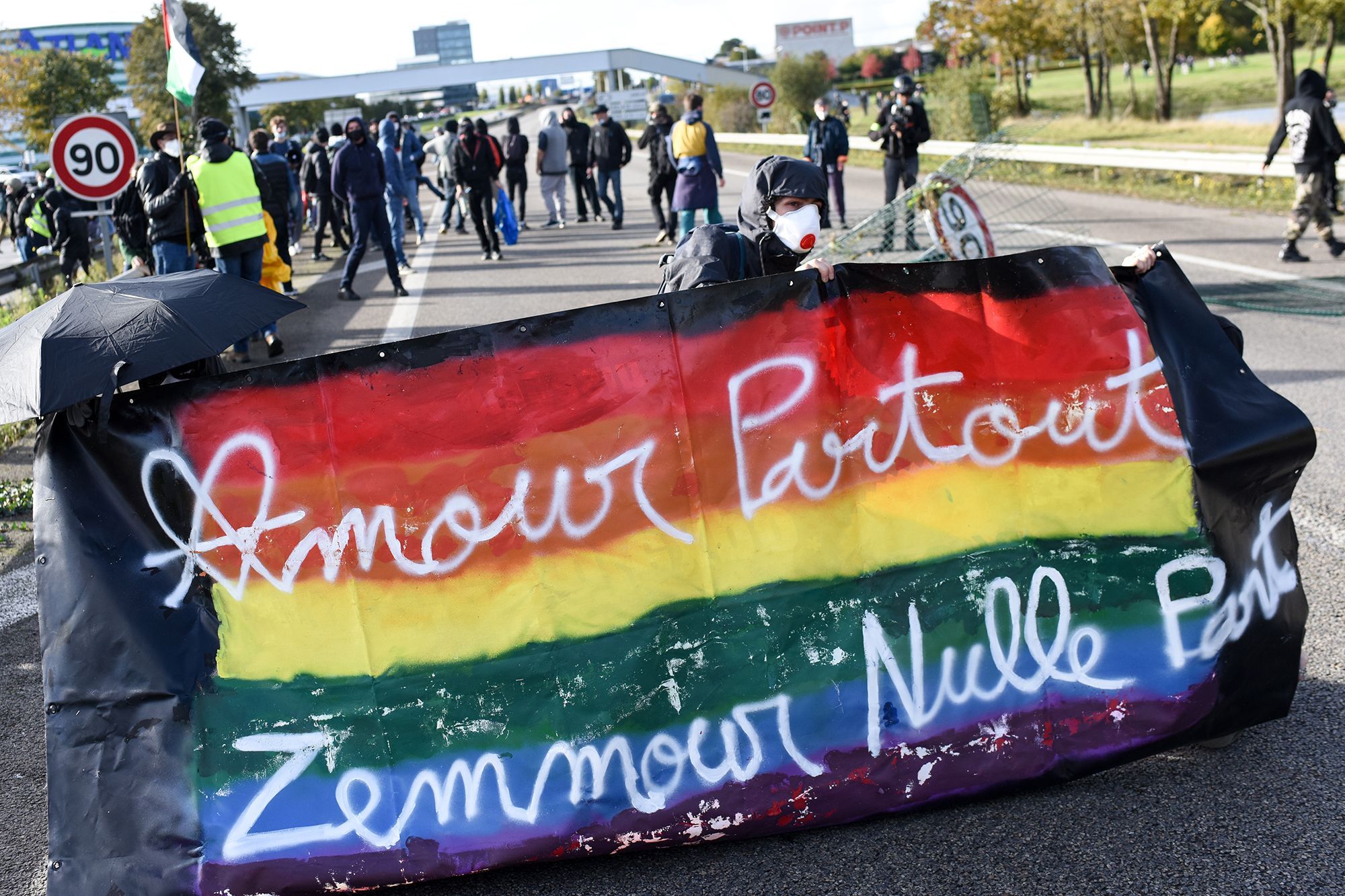 A protester hides behind a banner reading 'love everywhere, Zemmour nowhere' in Saint-Herblain, near Nantes, western France, on October 30, 2021, during a rally against the visit of the French far-right media pundit Eric Zemmour. - The French far-right media pundit Eric Zemmour visits Nantes' Zenith Metropole indoor arena on October 30, 2021 as part of his promotional tour for his book "France hasn't said its last word". (Photo by Sebastien SALOM-GOMIS / AFP)