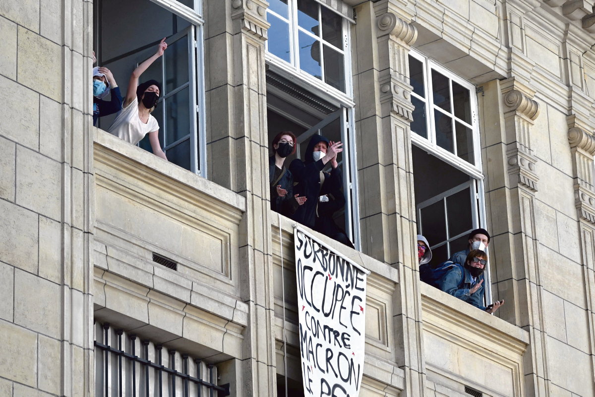 Students gestures in front of a banner reading "the Sorbonne occupied against Macron and Le Pen and their world" at the Sorbonne University in Paris on April 14, 2022,  as they stage a protest ten days ahead of the second round of France's presidentialele election. - Several hundred students mobilised on April 14, 2022 in Paris and Nancy, blocking university buildings to make their voices heard between the two rounds of the presidential election and to raise awareness of ecological and social issues. (Photo by EMMANUEL DUNAND / AFP)