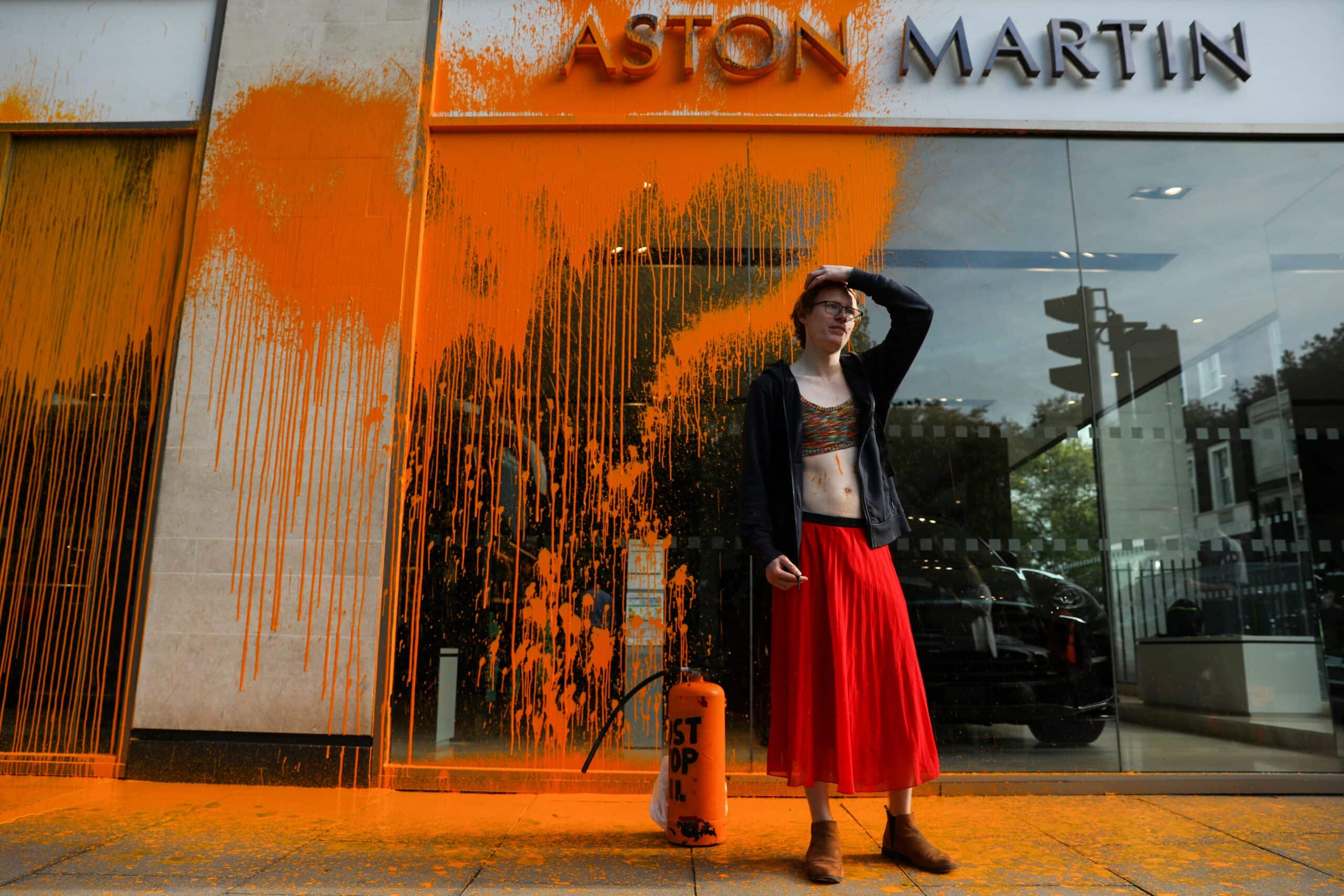 A member of the environmental activist group Just Stop Oil reacts after spraying orange paint on the window shop of the Aston Martin car show room, in central London, on October 16, 2022 as part of a series of actions. - Just Stop Oil, which wants an end to new fossil fuel licensing and production, are involved in a month-long series of protests in central London. (Photo by ISABEL INFANTES / AFP)